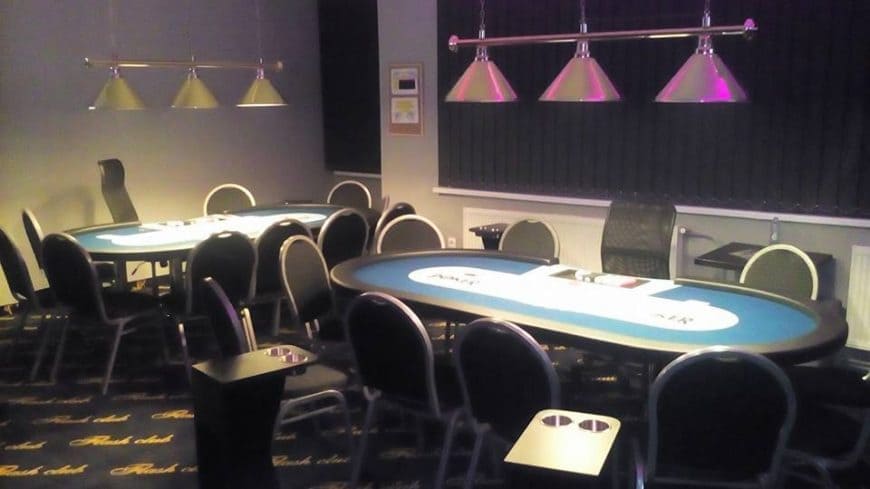 Pusta sala pokerowa z niebieskimi stołami i wiszącymi lampami
