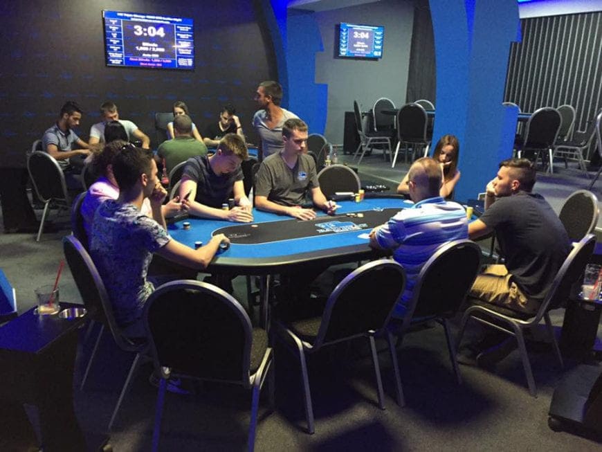 Sala pokerowa z graczami przy stole i ekranami wyników