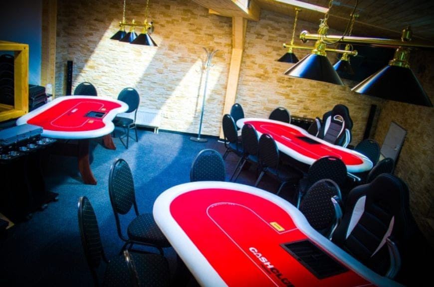 Sala pokerowa z czerwonymi stołami i kamienną ścianą