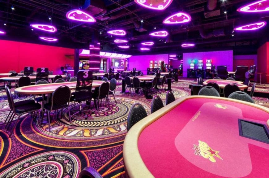 Szeroka sala pokerowa z różowymi neonami i wieloma stołami